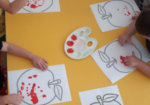 Dzieci palcem zamoczonym w farbie robią kropki na jabłku
